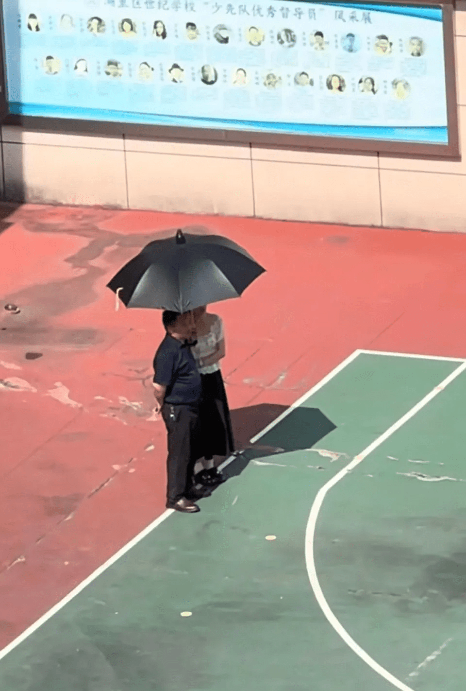 一名女教師烈日下為男子撐傘遮陽,引發「討好校領導」質疑。 一名女教師烈日下為男子撐傘遮陽,引發「討好校領導」質疑。