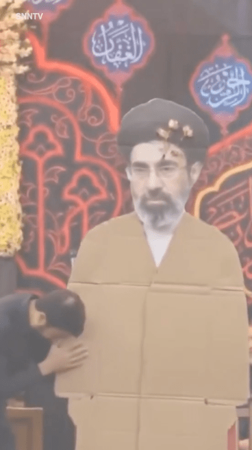 這塊代表穆傑塔巴的紙牌被抬上舞台中央，現場數以十萬計的民眾一邊揮舞伊朗國旗，一邊高喊口號，表達絕對效忠。《SNN TV》新聞畫面截圖