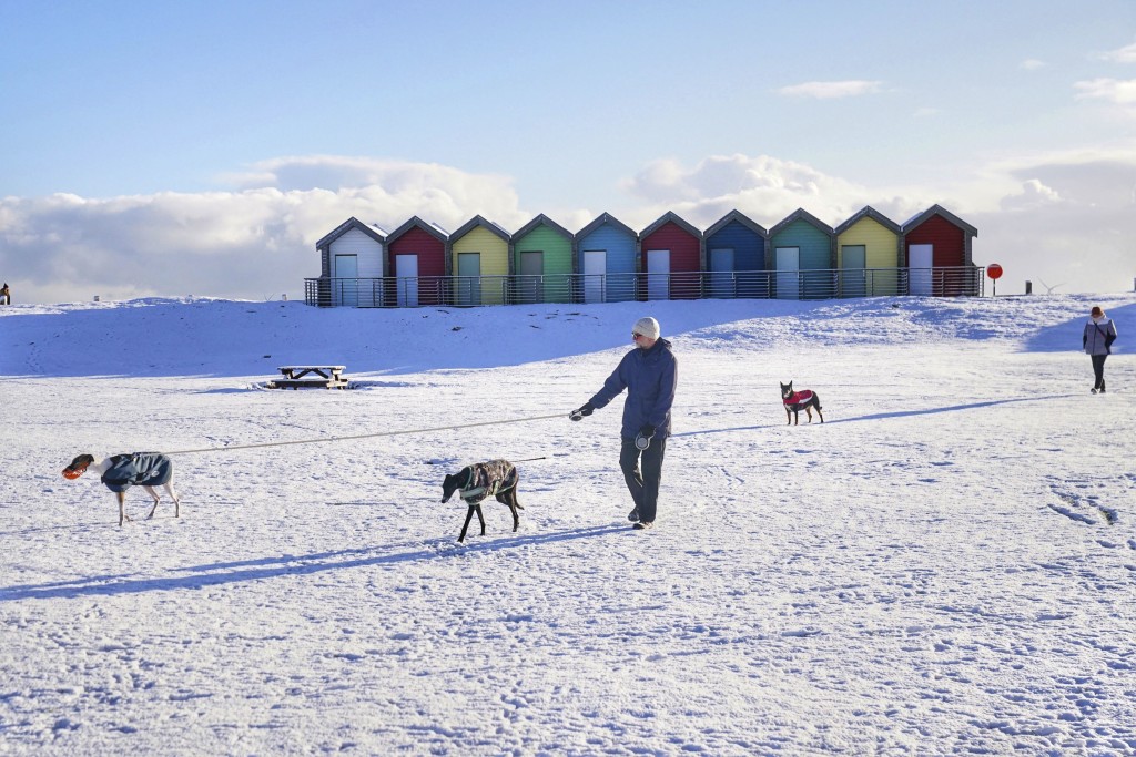 民众在英格兰东北部布莱斯的海滩小屋旁的雪地里遛狗。AP