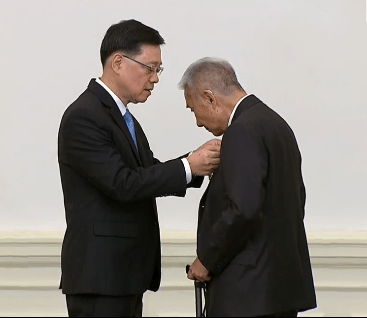 李家超向梁智仁頒發大紫荊勳章。港台FB影片截圖