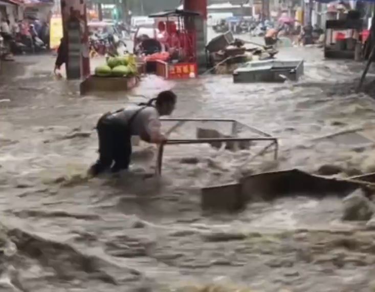 陕西长安区韦曲老街积水严重，有人浸在积水中企图保住被冲走的财物。