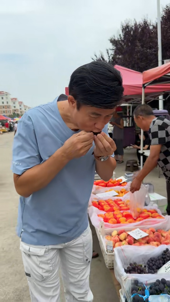 李子雄在水果档前试食大黑提。