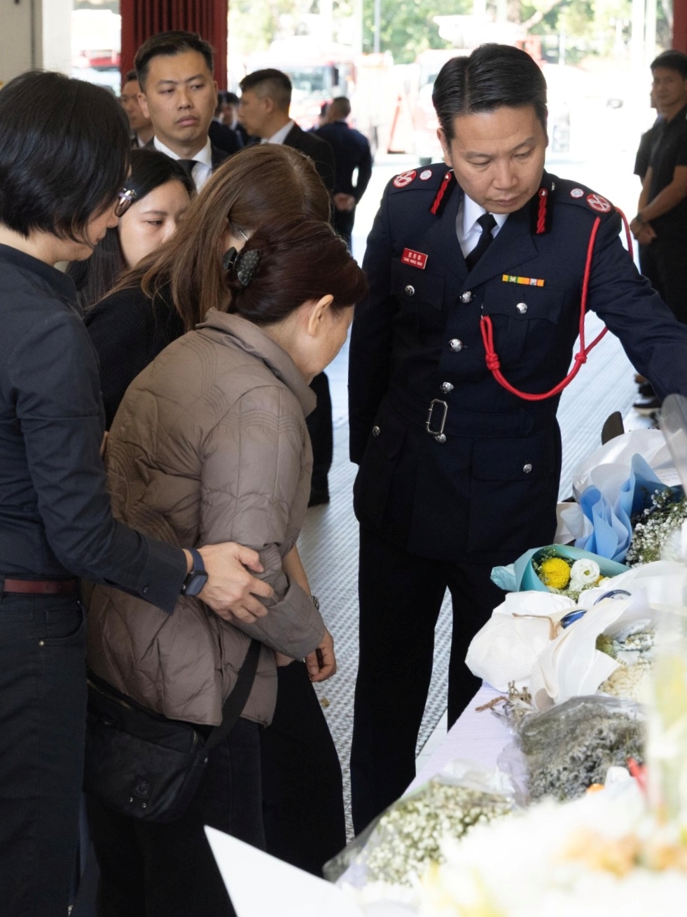 消防處助理處長（新界北）鄧榮華（右一）與何偉豪家屬觀看市民致送的鮮花和心意卡。