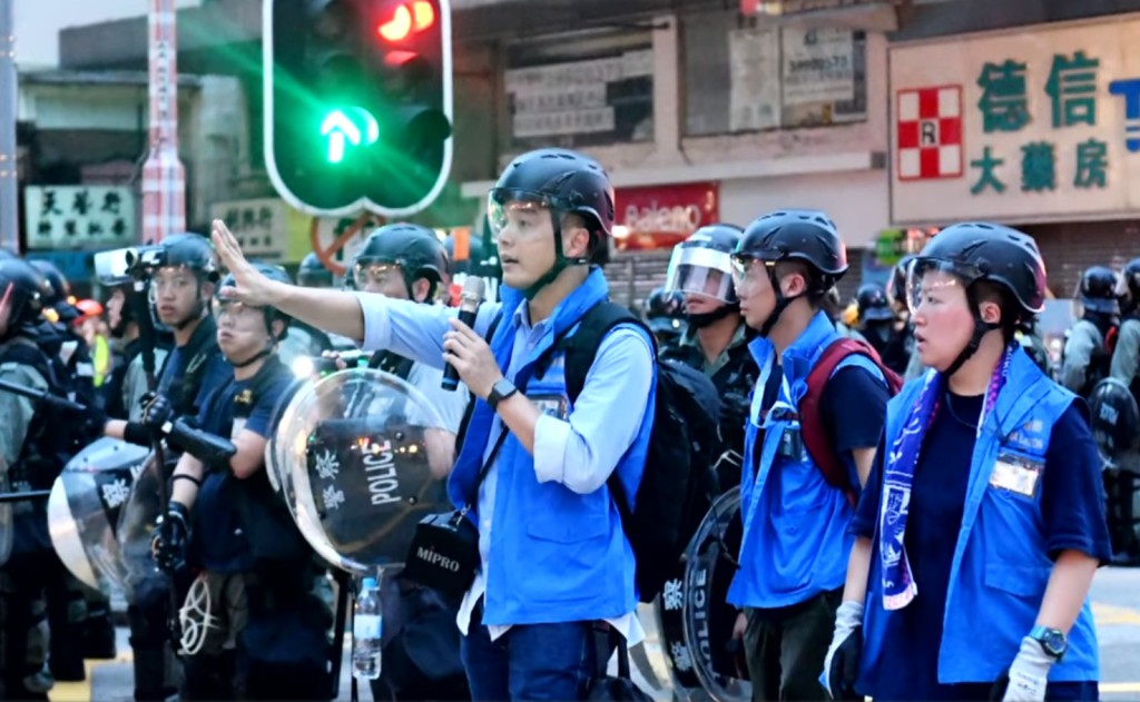 平日另一個工作,就是穿起藍背心到示威現場,要求記者給予「工作距離」給予警方。影片截圖