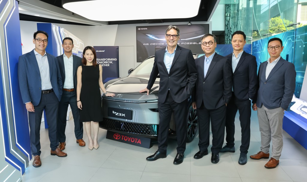 A group of seven people, including a woman in a black dress, stand beside a Toyota bZ3X electric vehicle in a modern showroom, highlighting Hong Kong's leading position in Asia-Pacific for high acceptance and ownership of new energy vehicles.