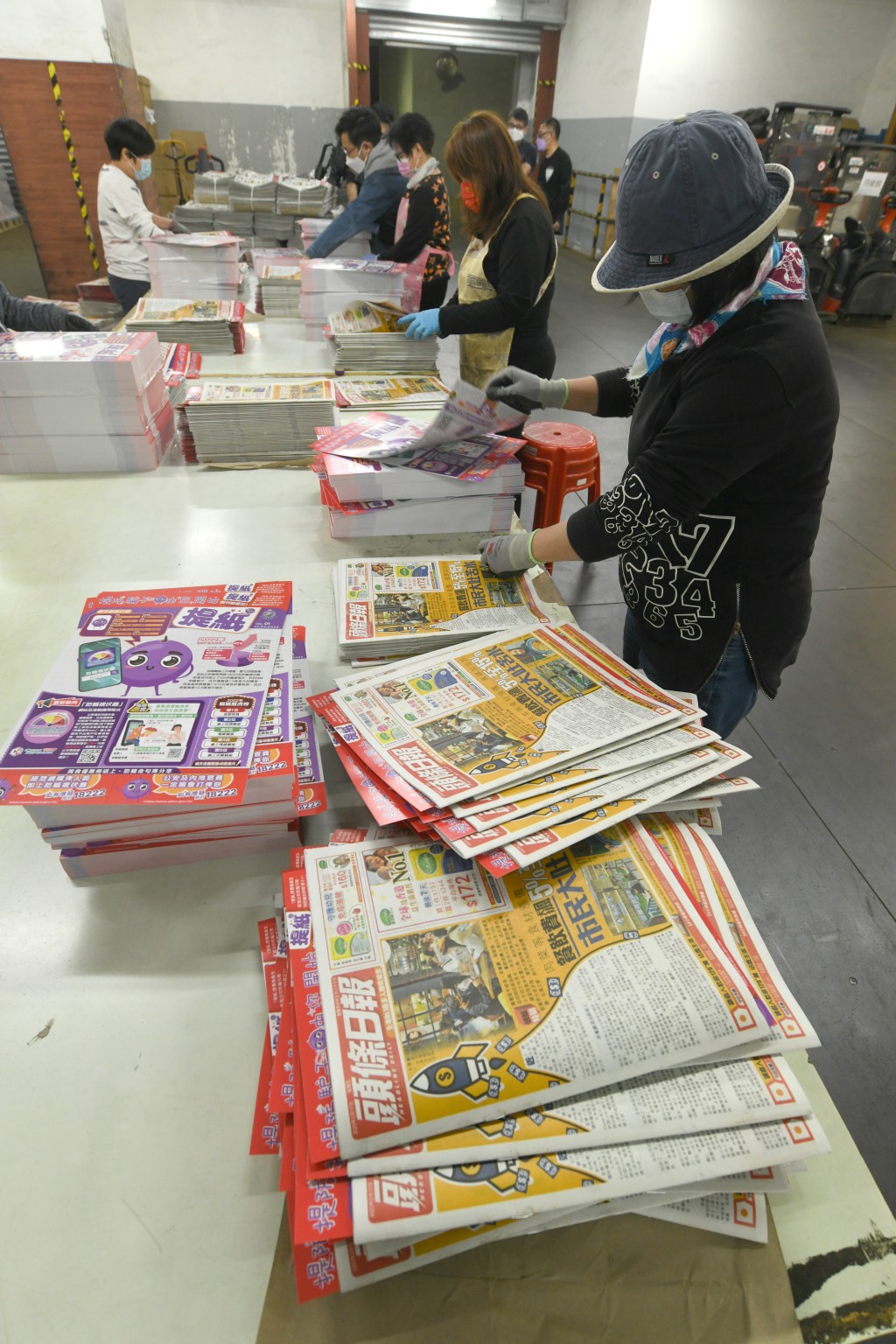 印製工人將「提紙」加進兩份免費報紙內。