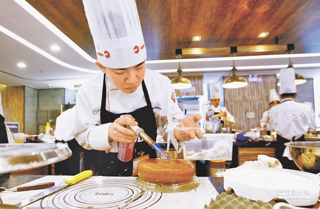 焙烤職業技能競賽上海賽區比賽，選手用噴火筒為其製作的冰上芭蕾裝飾蛋糕加固。新華社