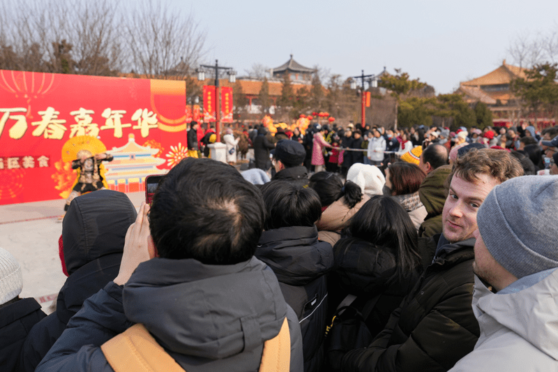 在北京景山公園，來自美國的遊客薩姆（右二）和同伴扎克（右一）欣賞公園內萬春嘉年華上的川劇變臉表演。 新華社