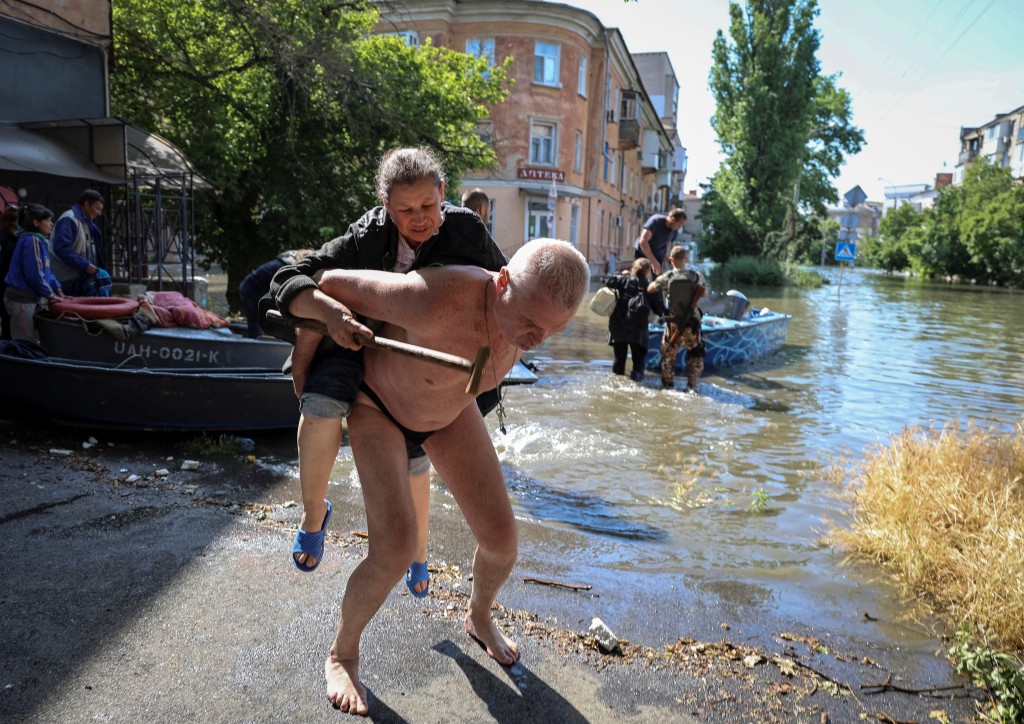 當地居民幫助從洪水氾濫的地區疏散一名婦女。路透社