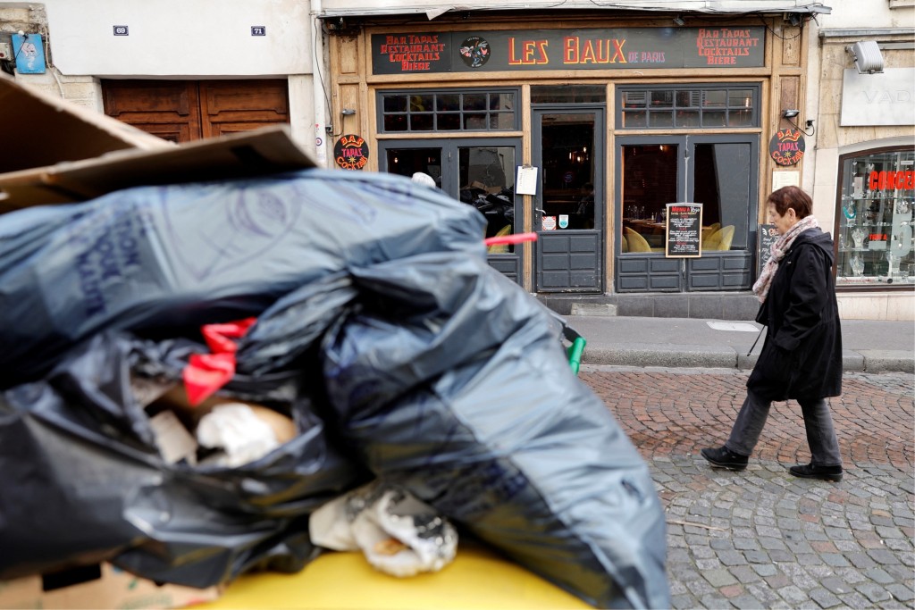 法國清潔工罷工10日，路人經過巴黎一處堆至滿瀉的街頭垃圾桶。 路透社
