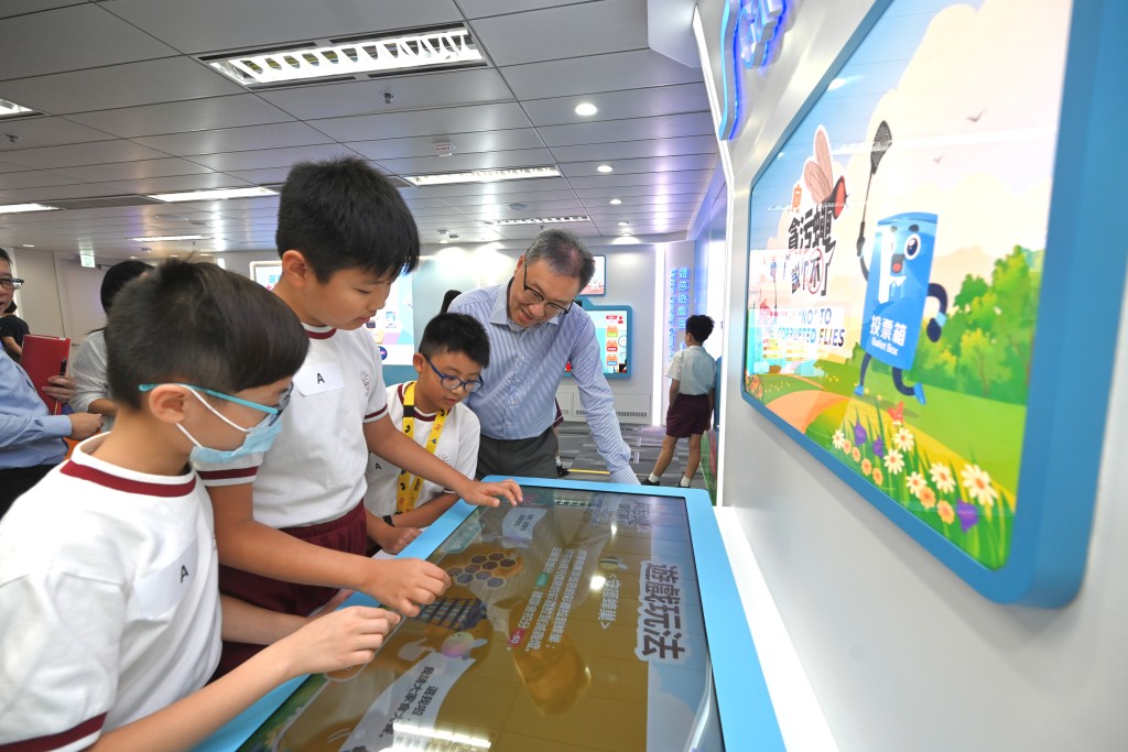 陆启康（右一）和学生试玩中心内全新设计的互动游戏——宣扬廉洁选举的「向贪污蝇说『不』」。政府新闻处图片