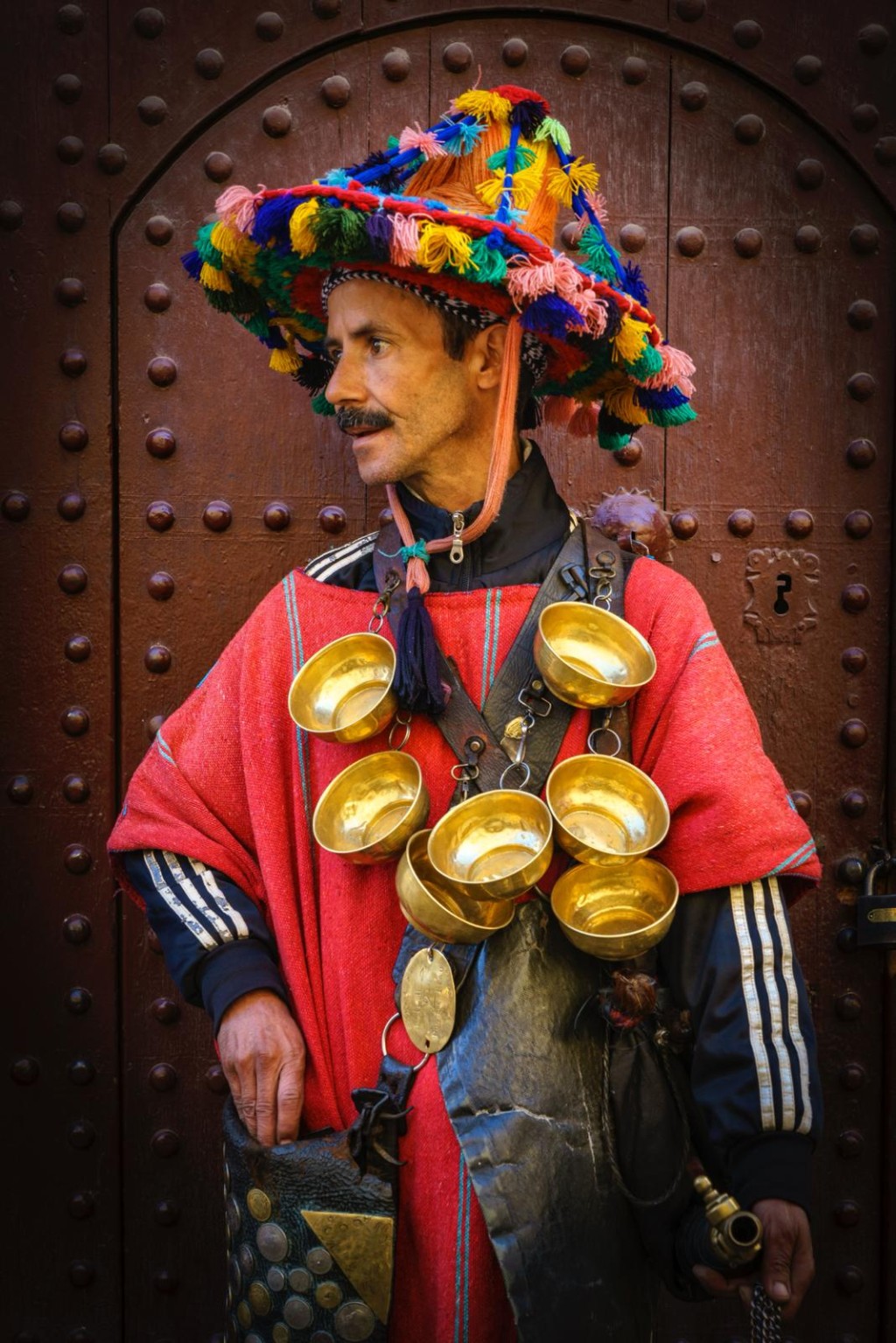 賣水人身上掛滿金光閃閃的銅水杯,配上掛在身後的羊皮水袋,站立在一扇古舊的門前。(圖片由馮敏如提供) 賣水人身上掛滿金光閃閃的銅水杯,配上掛在身後的羊皮水袋,站立在一扇古舊的門前。(圖片由馮敏如提供)