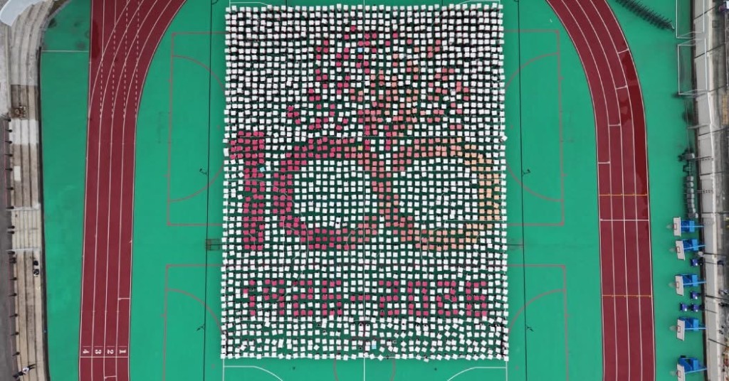 幼小中三部逾2,000名學生和教師拼出學校校徽和百年標誌的兩個巨大圖案，慶祝100周年校慶。（圖片來源：受訪者提供）