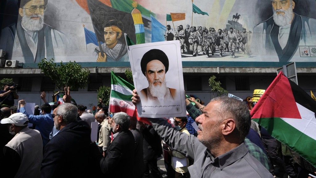 伊朗信众在一场反以色列集会中，高举已故革命创始人霍梅尼肖像、伊朗国旗和巴勒斯坦国旗。 美联社
