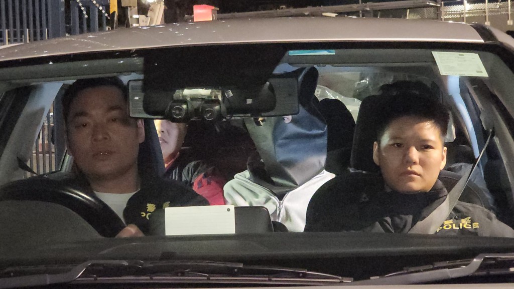 24日凌晨零時左右，其中一名被捕男子被帶上頭套，在重案組人員押解下，由便裝警車載離田心警署。黎志偉攝