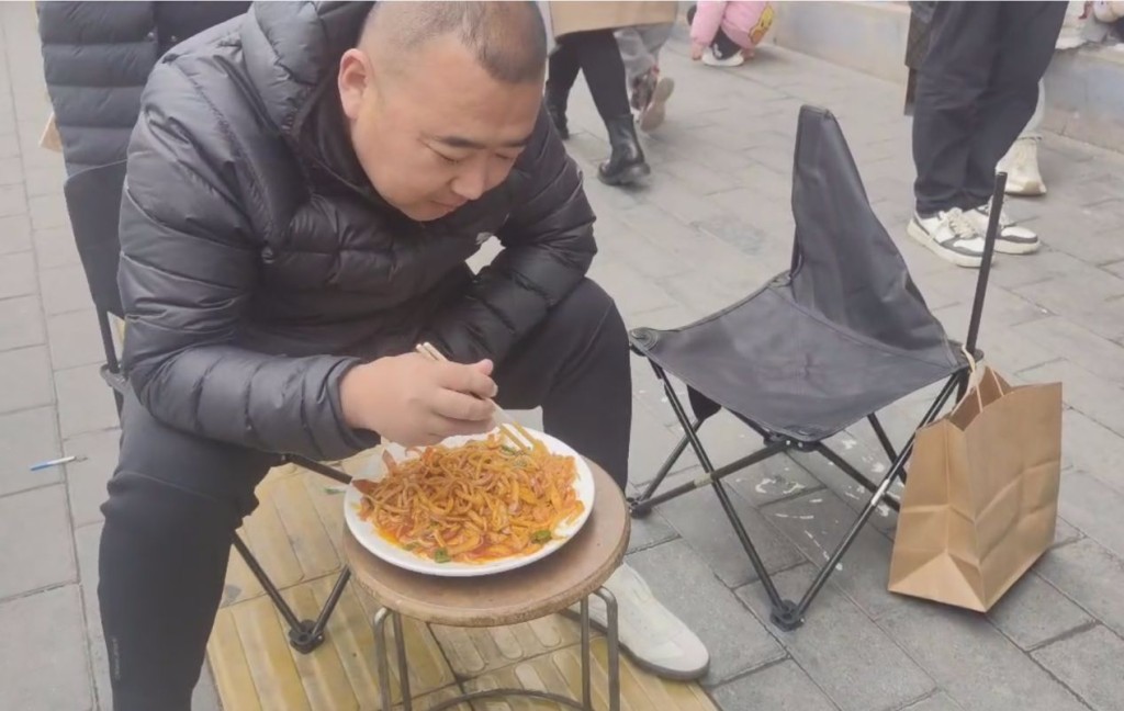 天水古城附近一家麻辣烫店门口，一位来自陕西商洛的男子边吃面边排队，当时该男子已排队2小时。 澎湃新闻