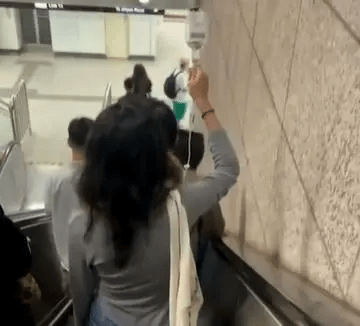 女生被拍到在住地铁月台的扶手电梯上，边吊盐水边上路。
