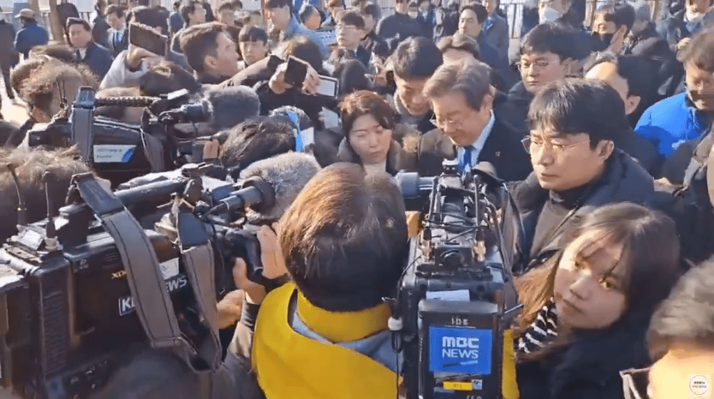 李在明造訪釜山加德島新機場預定興建地時被傳媒包圍。 網片截圖
