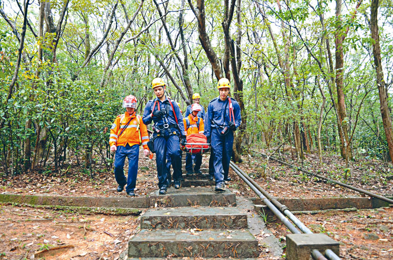 救援人員冒雨抬着墮坡受傷女子落山。