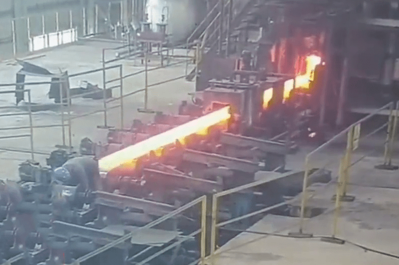工人身后一根烧得火红的钢条产出，愈来愈接近。