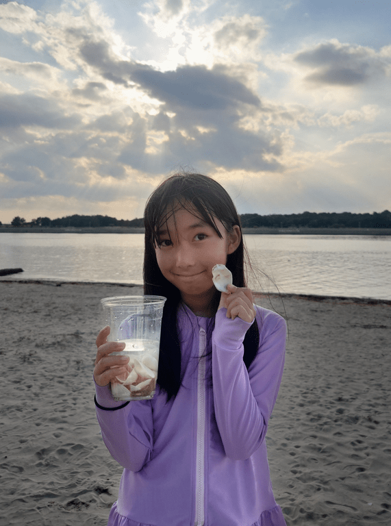 平田琉七在沙灘展示收集到的貝殼，笑意盈盈。