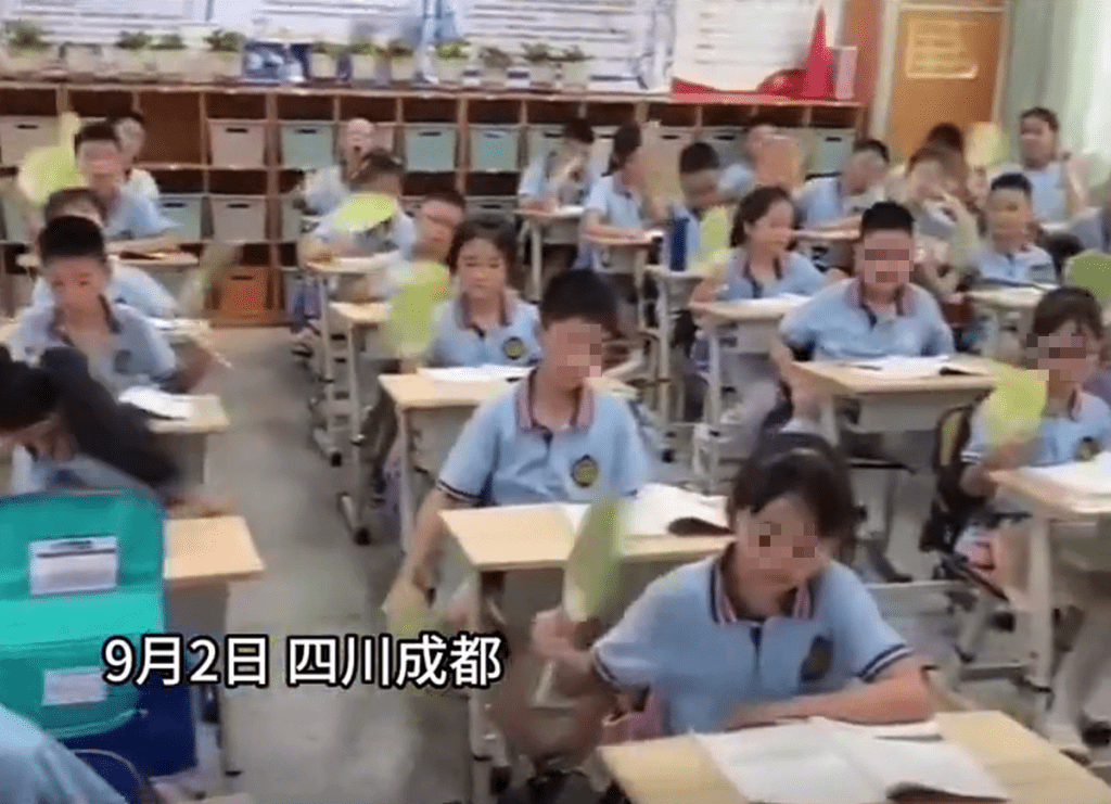 成都一小学学生满头大汗，一直摇著扇子降温。