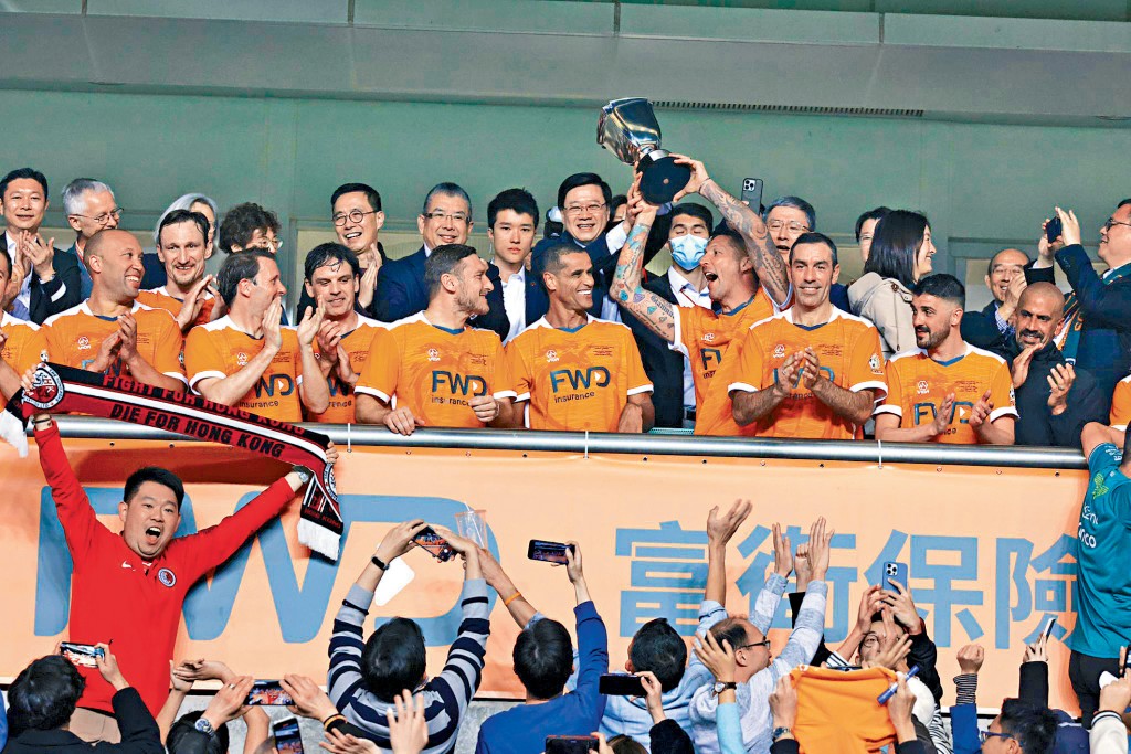 特首李家超與勝出的世界明星隊在頒獎台上，齊齊高舉獎盃，充滿歡樂氣氛。