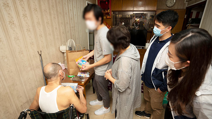 懲教署和警務處工作人員(穿風褸者)與更生人士及其家人一同探訪居住在灣仔區的殘障長者,並送贈「端午祝福包」。