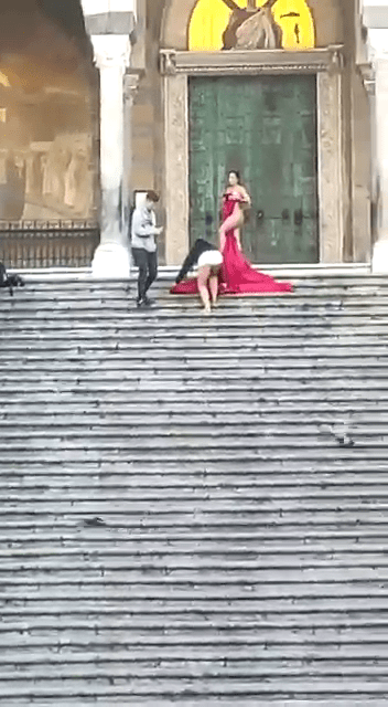 女游客拉着一块红布遮掩重要部位并摆出撩人姿态，在大教堂门口前的阶梯拍裸体写真。
