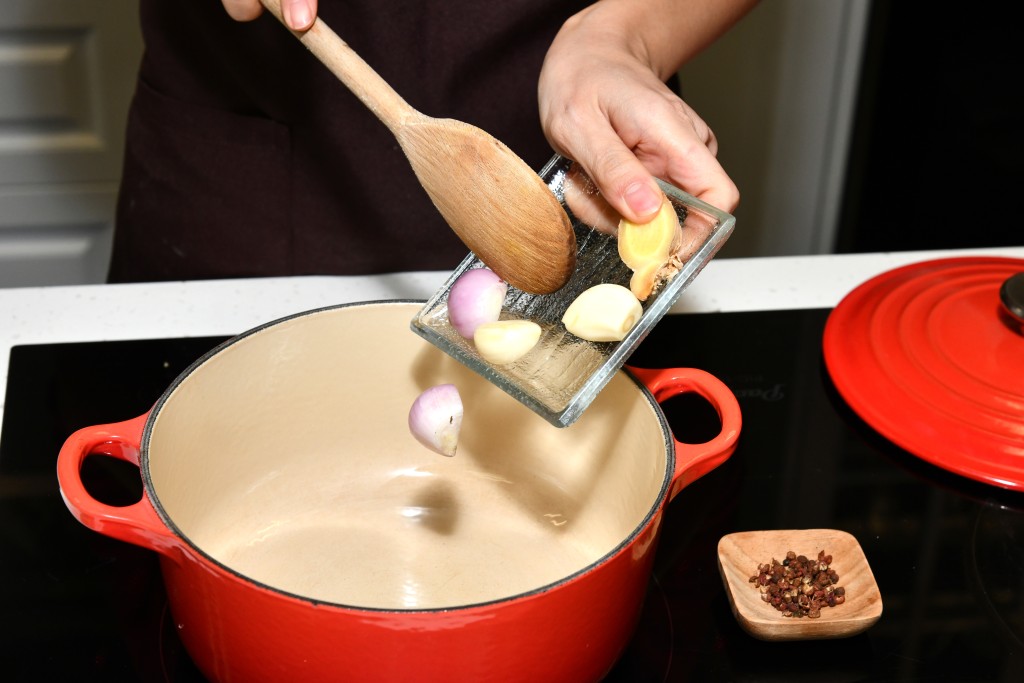 Step 5: 鍋內燒熱油，加入蒜頭、乾 葱、花椒、豬手和南乳炒香。Heat oil in a pot, add the garlic, shallot, Sichuan peppercorn, pork knuckles and red fermented bean curd, stir-fry until fragrant.