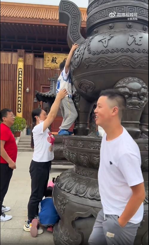 深圳弘法寺有遊客爬上大香爐撿拿其他遊客扔進去的香油錢。