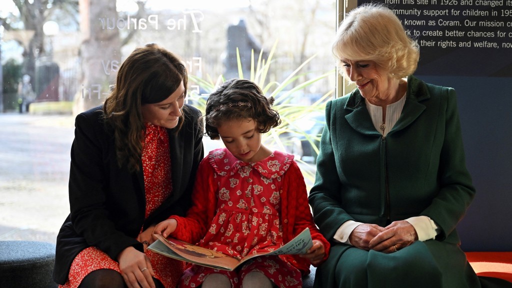 卡米拉推动儿童识字。图为她参观慈善机构时，与一名女孩和养母一起看书。 路透社