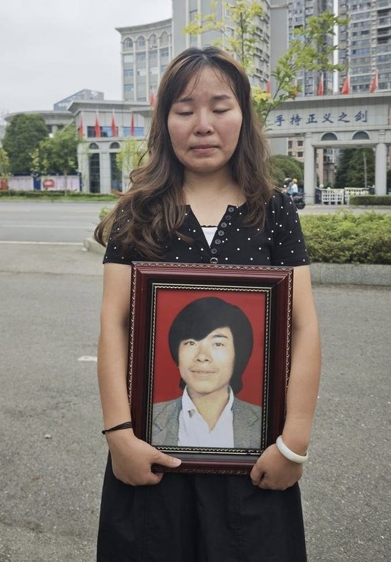李某平女儿长大成人，抱着父亲遗照到法院听审。 