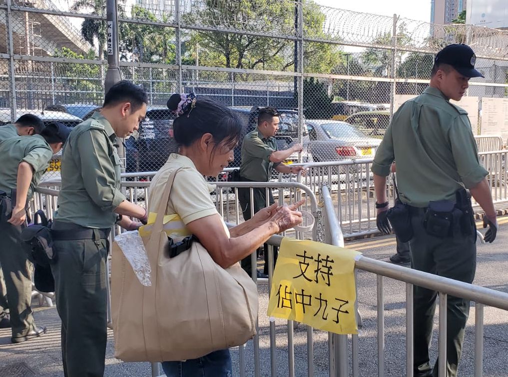 一名女子下午將手持的「支持佔中九子」黃色紙張貼在收押所外的鐵馬上。