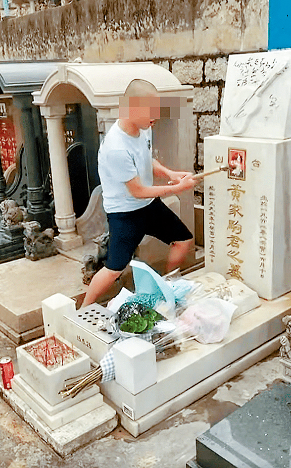 兩名青年在黃家駒墳前拍片，一人其後拿鐵槌扑爆家駒遺照。