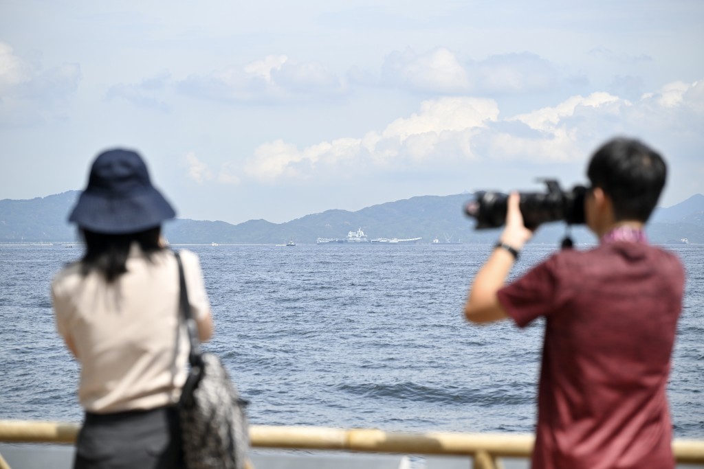 不少市民遊客在堅尼地城海傍遠眺山東艦。