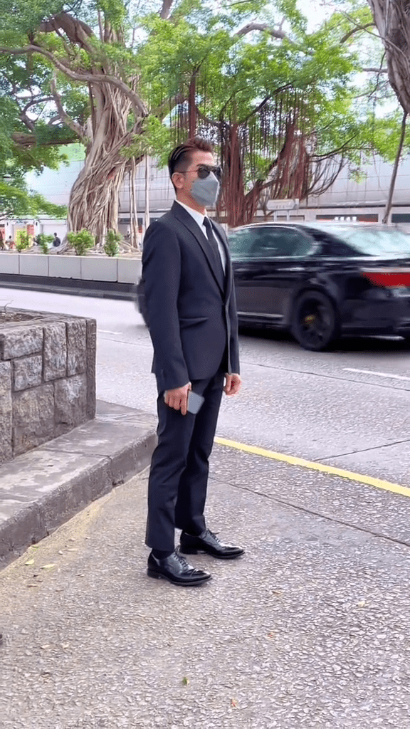 郭富城一身黑色西装站在马路边的停车处等车，腰骨挺直，充份展现出巨星气场。