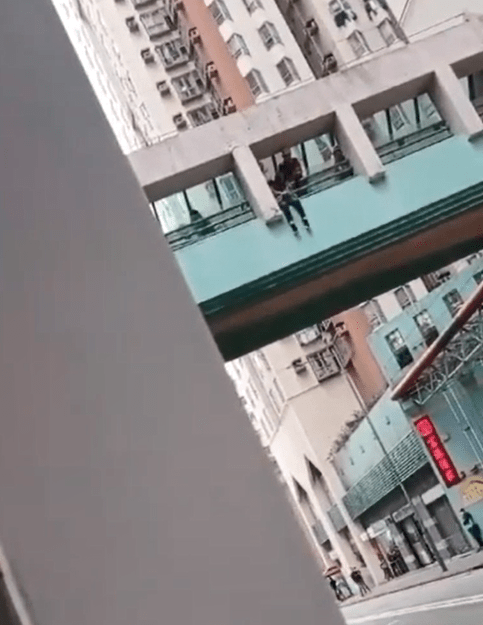 女子攀過天橋欄杆危坐壆邊企圖躍下。讀者提供影片截圖