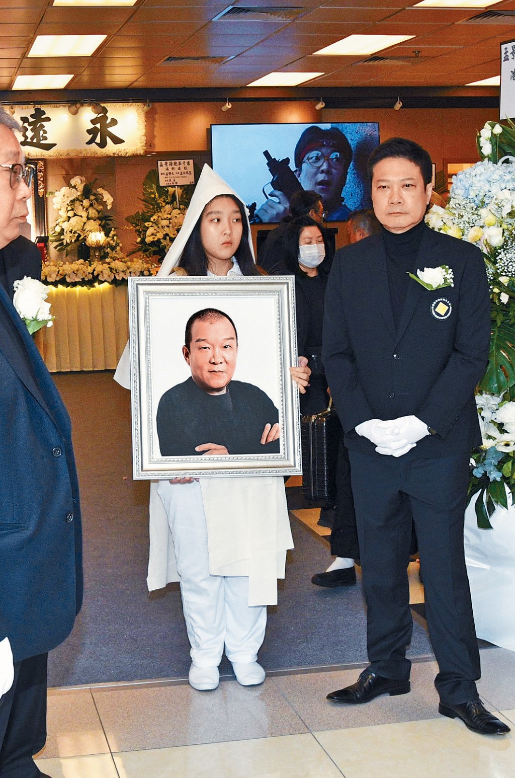 孟海女兒捧着父親遺照步出靈堂，好友錢嘉樂全程在旁協助。