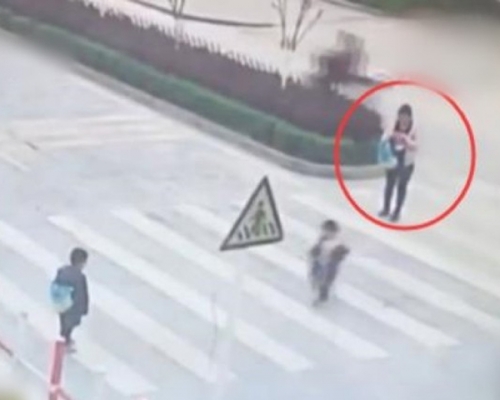 两名孩子在马路上来回奔跑，该名母亲却只顾玩手机。 网图