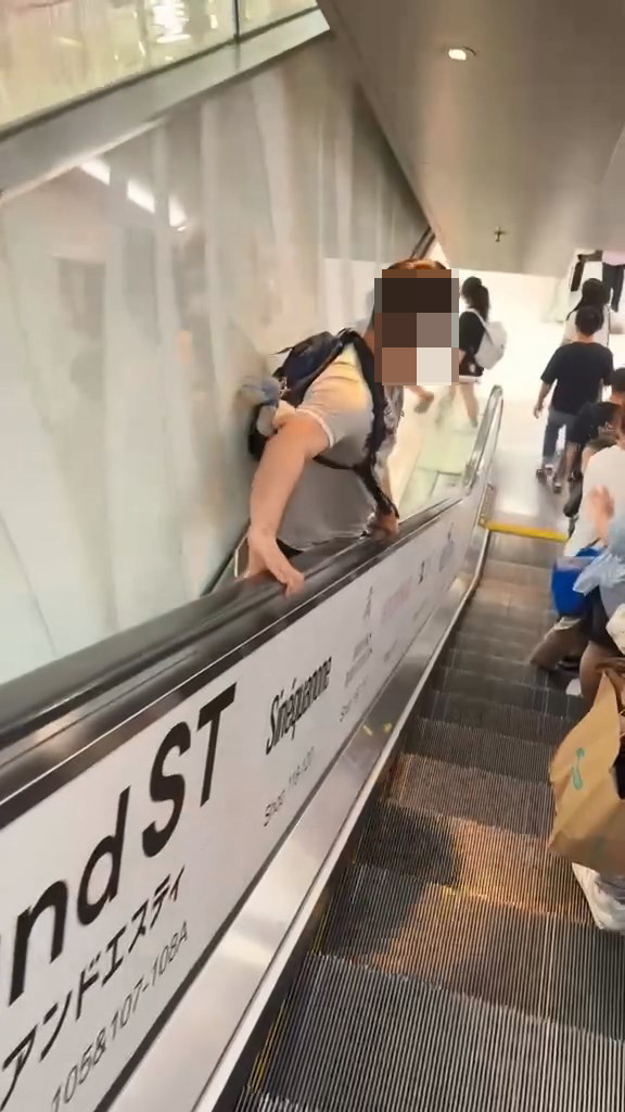 男子翻越玻璃欄杆,爬落扶手電梯中間的銀色蓋板,之後沿著蓋板慢慢爬行到下一層。Threads@showerrrjun片段截圖 男子翻越玻璃欄杆,爬落扶手電梯中間的銀色蓋板,之後沿著蓋板慢慢爬行到下一層。Threads@showerrrjun片段截圖