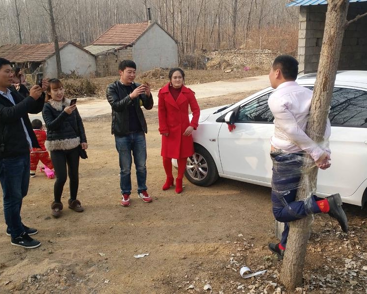 新郎被朋友用透明封箱胶纸绑在离家不远的杨树上。