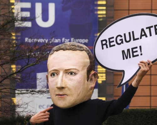 抗爭者戴著Facebook CEO朱克伯格的面具，在歐盟委員會外面舉著Regulate me標語。ap圖