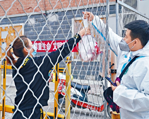 ■哈爾濱穿防護服的快遞小哥為居民送貨。