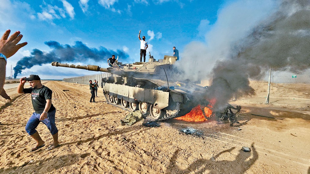 加沙地帶的巴人在一輛損毀的以軍坦克旁慶祝。 