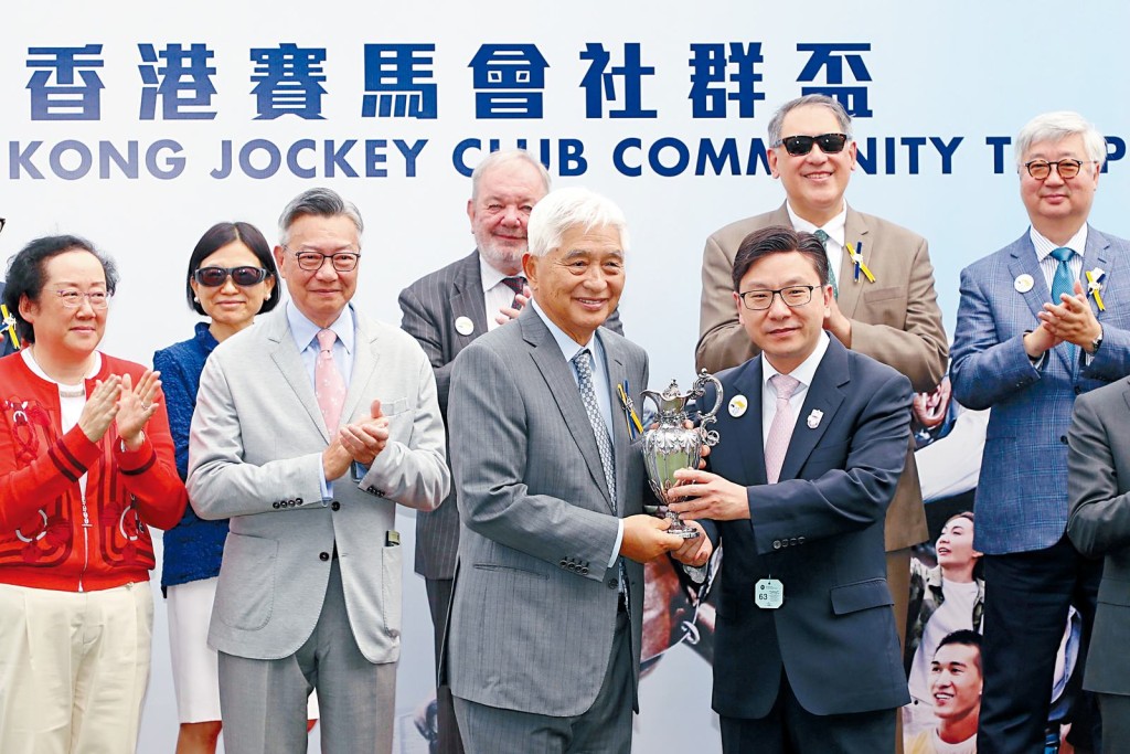 局長孫玉菡（前排右）於「香港賽馬會社群盃」賽事後，頒發獎盃予頭馬「金馳」的馬主榮智健（前排左）。賽事頒發的獎盃已有超過170年歷史，由收藏家雷剛捐贈，以表揚馬會對社會的貢獻。