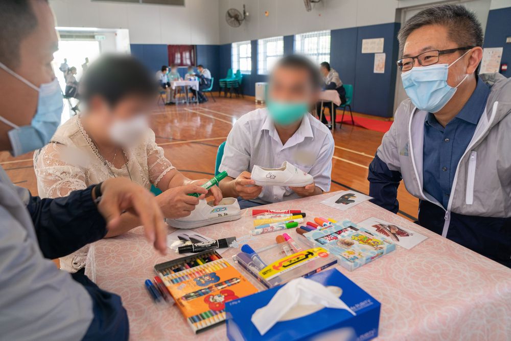 警務處副處長蕭澤頤(右一)鼓勵青少年在囚人士與母親在小鞋子上繪畫。