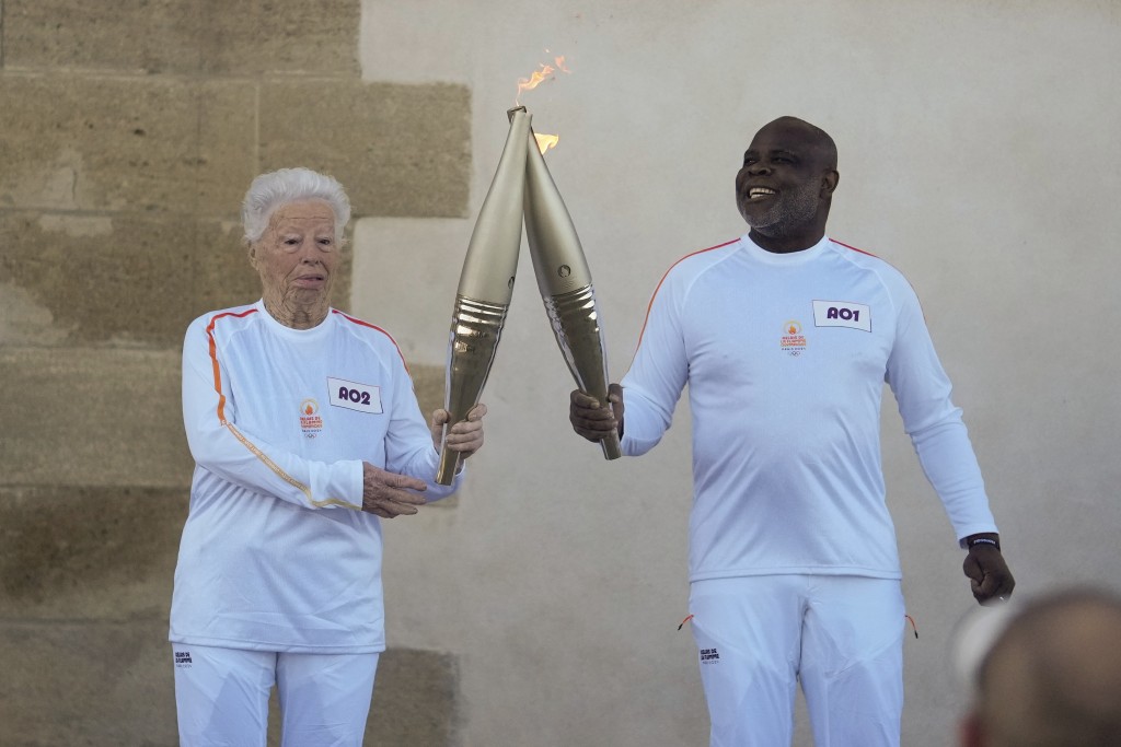 法国火炬手科莱特·卡塔尔多（左）和巴塞尔·博利在法国南部马赛举行的奥运火炬传递第一阶段中进行火炬交接。 AP