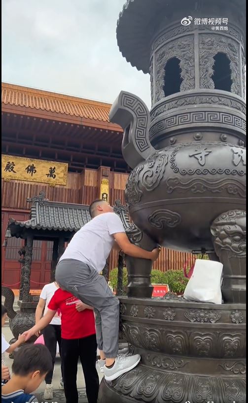 深圳弘法寺有遊客爬上大香爐撿拿其他遊客扔進去的香油錢。
