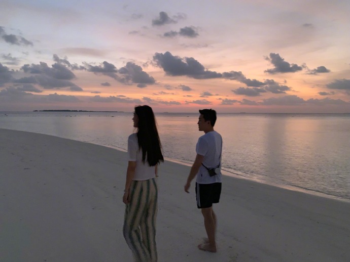 兩人在夕陽美景下漫步沙灘。